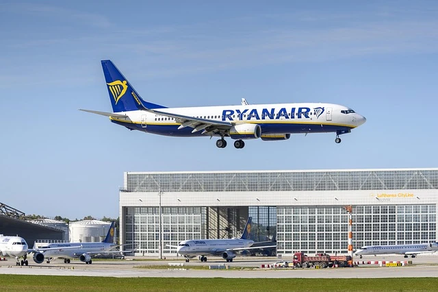 Avión de Ryanair aterrizando en un aeropuerto europeo con hangares de Lufthansa al fondo.