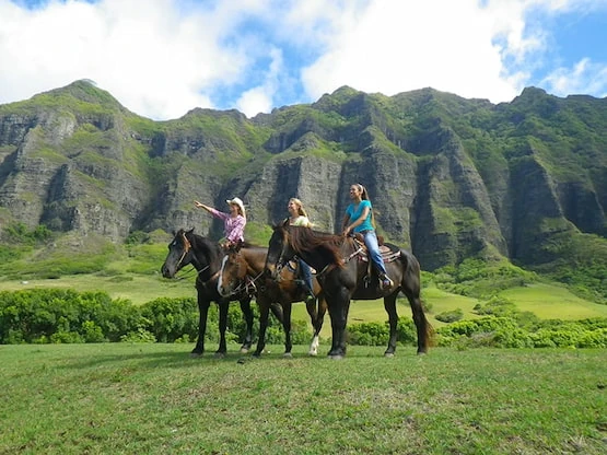 Cabalgata en Kualoa Ranch, una de las experiencias más populares para explorar el paisaje hawaiano Turistas montando a caballo en las verdes praderas de Kualoa Ranch, Hawái
