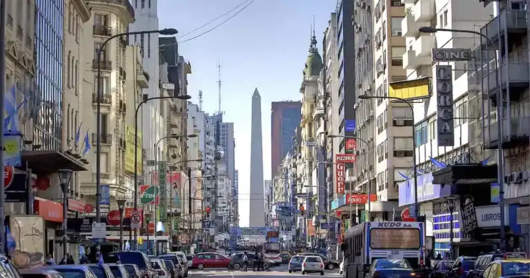 Avenida urbana con edificios y obelisco al fondo bajo cielo azul