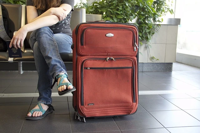 Esperando el vuelo con maleta de tamaño adecuado Viajero esperando con una maleta roja antes de embarcar