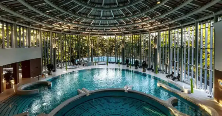 Spa con múltiples piscinas cubiertas, techo de cristal y vistas boscosas