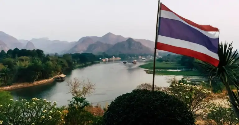 Paisaje natural de Tailandia con río, montañas y bandera tailandesa en primer plano