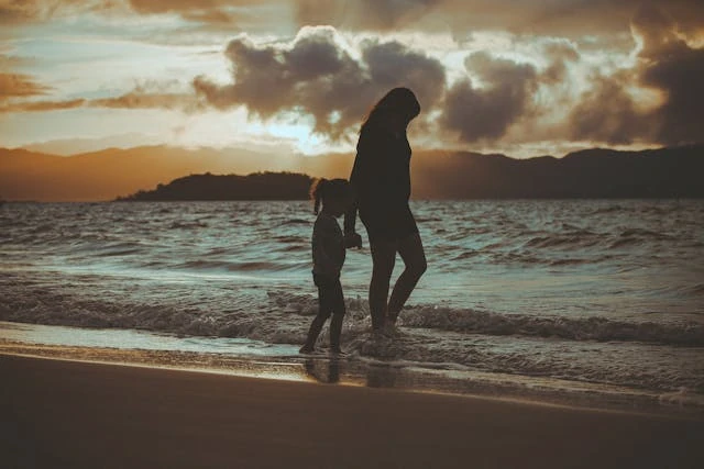 Mujer y niña caminando descalzas por la playa al atardecer.