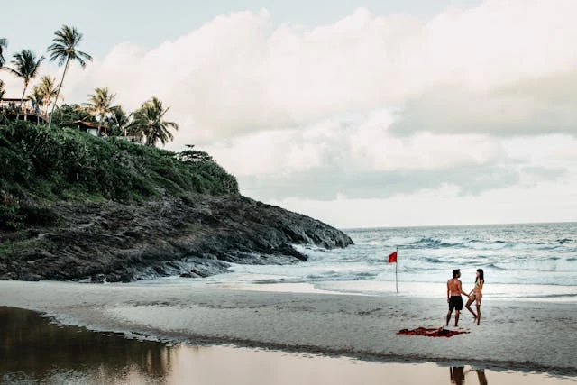 Pareja disfrutando de una playa tropical con bandera roja y fondo rocoso.