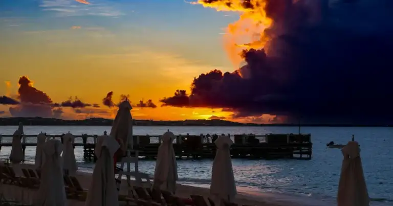 Puesta de sol sobre agua con personas en primer plano y pier de madera