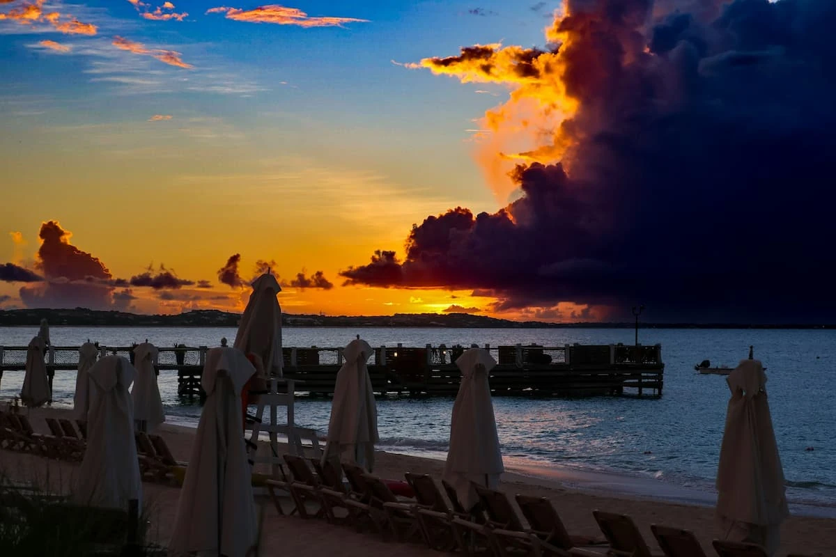 Puesta de sol sobre agua con personas en primer plano y pier de madera