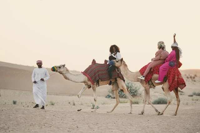 Turistas montando camellos en el desierto de Dubái durante un safari al atardecer