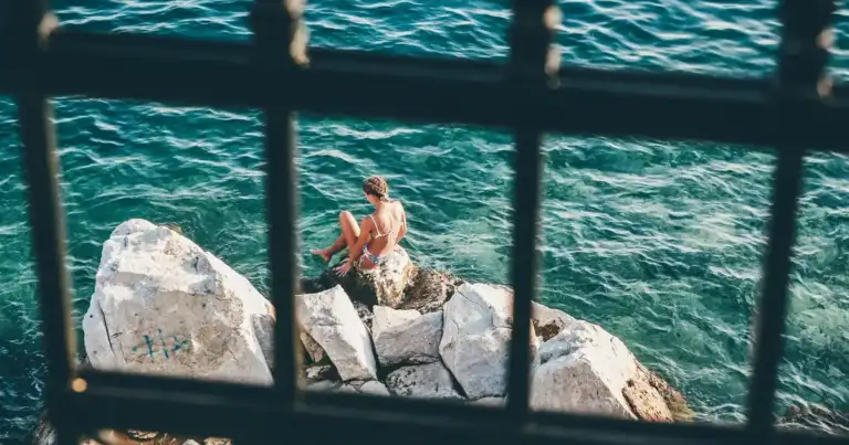 vista del mar a traves de una reja.Abajo una persona sentada en una piedra