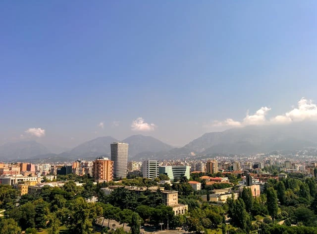 Vista panorámica de una ciudad con edificios modernos, zonas verdes y montañas al fondo.