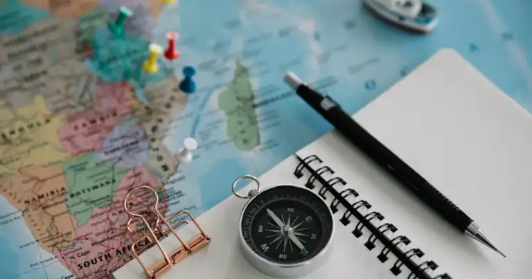 Mapa con chinches de colores, brújula, cuaderno y lápiz para planificar un viaje.