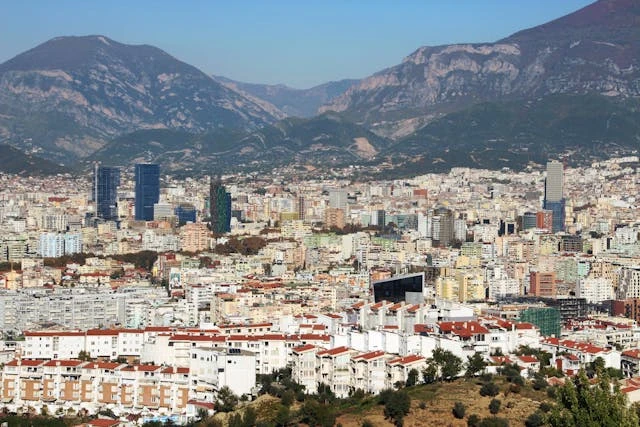 Panorámica de Tirana, Albania, con montañas de fondo y edificios modernos y tradicionales.
