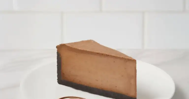 Porción de cheesecake de chocolate sobre plato blanco con decoración de salsa.