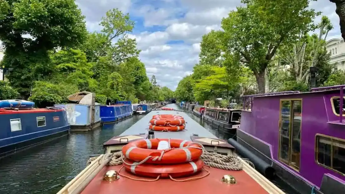 Vista desde un paseo en barco por el canal de Little Venice, con barcos narrowboats a ambos lados y árboles frondosos.