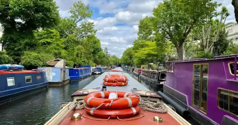 Vista desde un paseo en barco por el canal de Little Venice, con barcos narrowboats a ambos lados y árboles frondosos.
