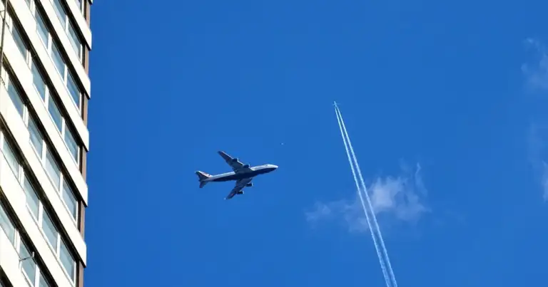 Avión sobrevolando edificio con cielo azul y estela de condensación