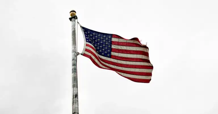 Bandera de Estados Unidos ondeando sobre un fondo gris claro.