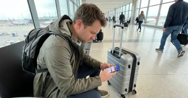 Viajero en el aeropuerto comparando precios de vuelos en su celular antes de comprar el ticket