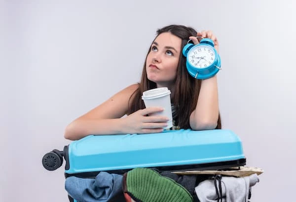 tien un vaso de café en su otra mano mujer joven con una valija a medio armar y un reloj en su mano