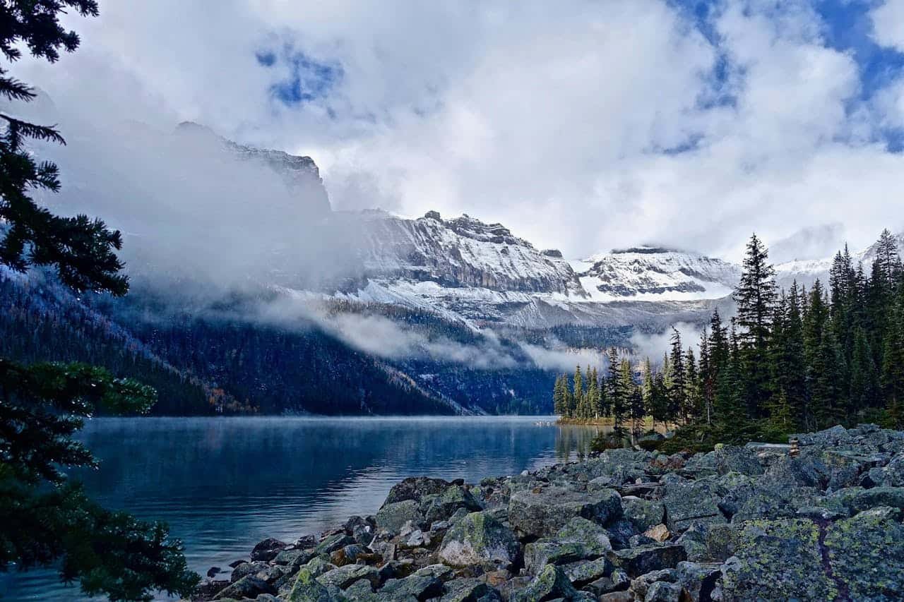 Lago rodeado de bosque y montañas nevadas en Alaska con nubes bajas sobre el paisaje