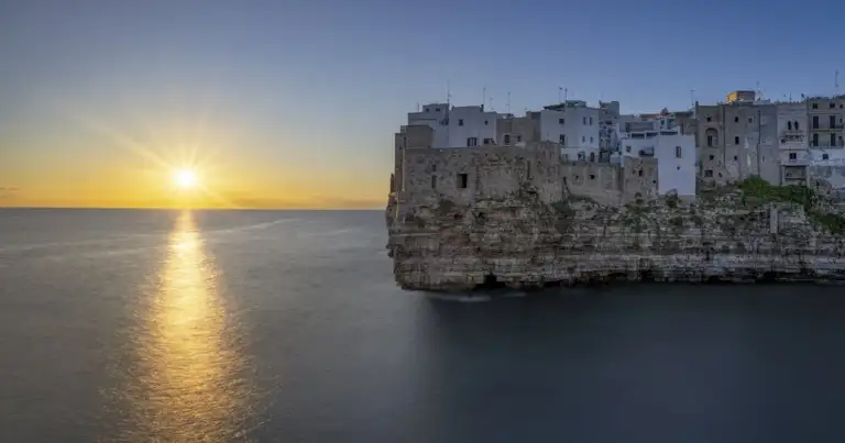 Polignano a Mare al atardecer con casas sobre acantilados frente al mar Adriático en Puglia, Italia.