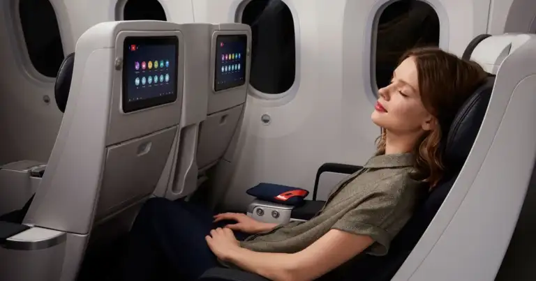 Pasajera descansando en asiento reclinable de avión con pantalla individual y mayor comodidad en premium economy