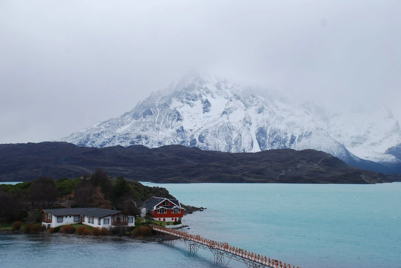 Lago de color turquesa con montañas nevadas y cabañas en la Patagonia chilena, una imagen que representa los paisajes ideales para unas vacaciones de invierno en Chile.