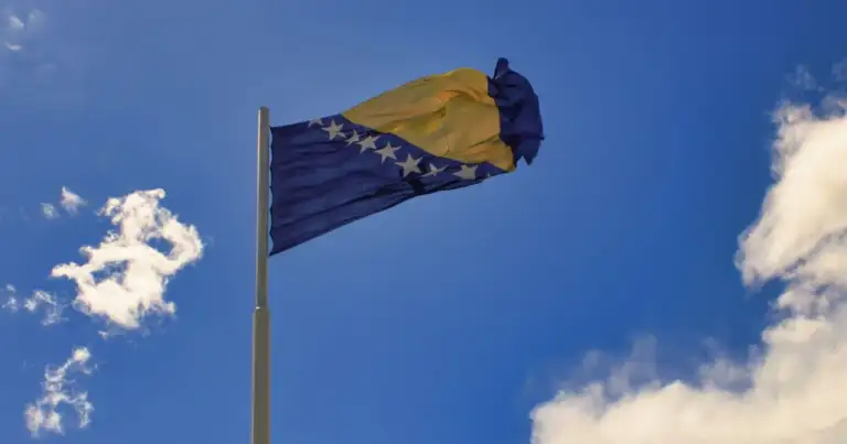 Bandera de Bosnia y Herzegovina ondeando sobre cielo azul, imagen útil para ubicar el país en los Balcanes.