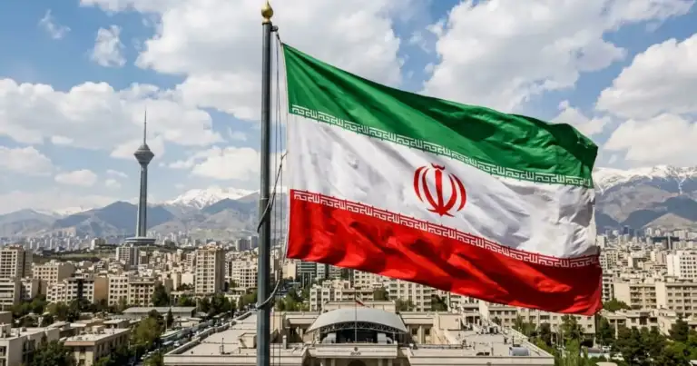 Bandera de Irán ondeando sobre Teherán, capital del país, con montañas al fondo y paisaje urbano.