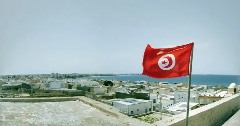 Bandera de Túnez ondeando sobre una ciudad costera junto al mar Mediterráneo.