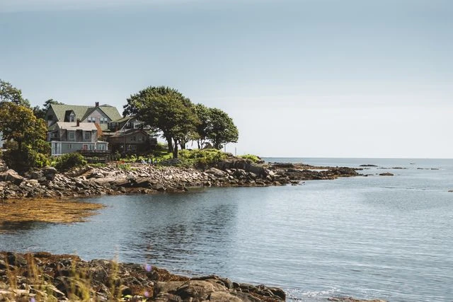 Casas junto a la costa rocosa de Nueva Inglaterra, con mar tranquilo y paisaje típico del noreste de Estados Unidos.