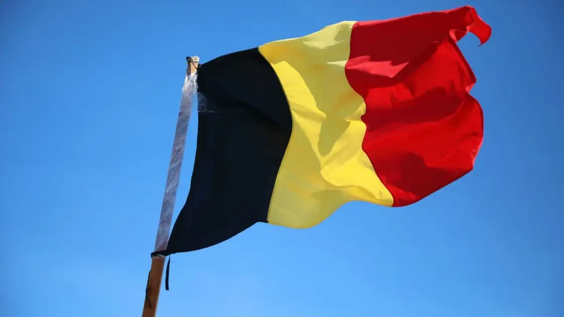 Bandera de Bélgica ondeando sobre cielo azul, imagen relacionada con una guía sobre dónde queda Bélgica en Europa.