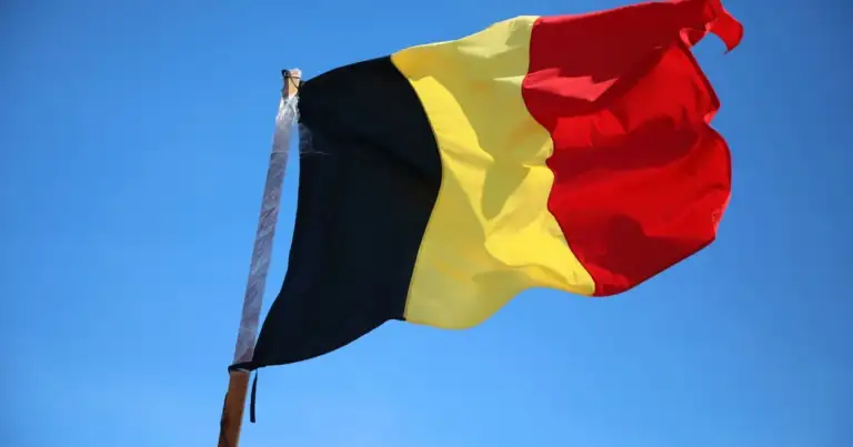 Bandera de Bélgica ondeando sobre cielo azul, imagen relacionada con una guía sobre dónde queda Bélgica en Europa.