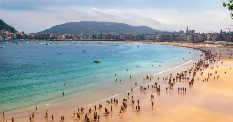 Vista panorámica de la playa de La Concha con bañistas, embarcaciones y el centro de San Sebastián frente a la bahía.