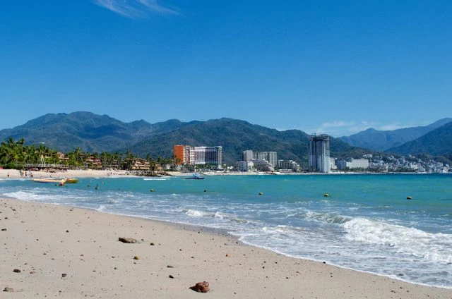 Playa de Puerto Vallarta con mar turquesa, hoteles frente a la costa y montañas de la Sierra Madre al fondo.