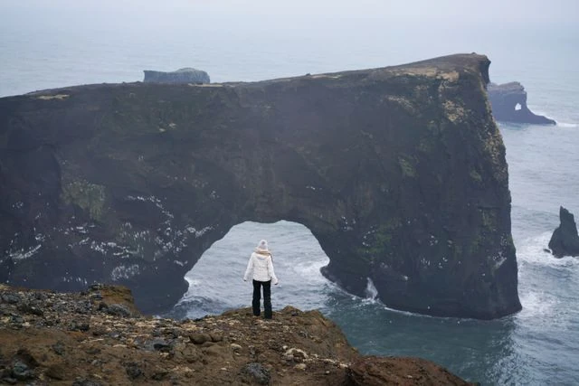 Viajera frente al arco natural de Dyrhólaey y los acantilados de la costa sur de Islandia.