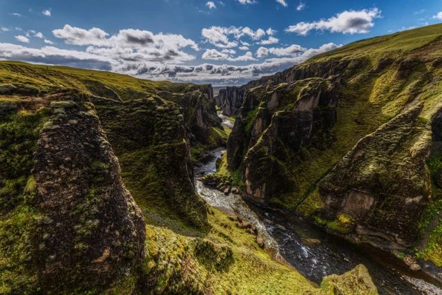 Cañón Fjaðrárgljúfur en una ruta de viaje por Islandia Cañón Fjaðrárgljúfur en Islandia, con paredes cubiertas de musgo y un río serpenteando entre las rocas.