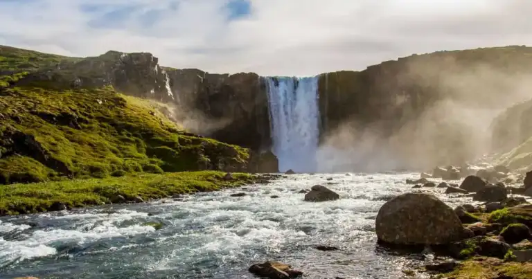 Cascada rodeada de campos verdes y un río en Islandia durante los meses de clima más templado.