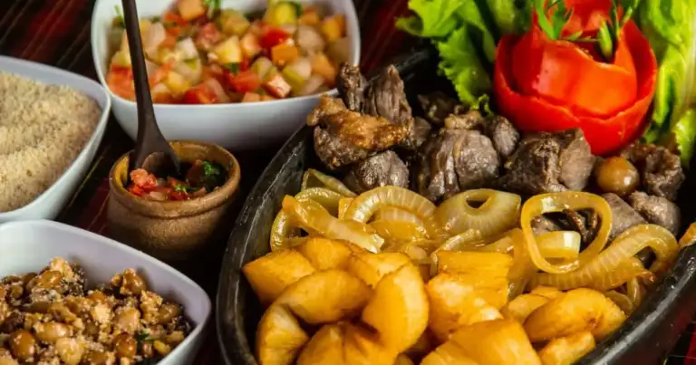 Plato de comida brasileña con carne, mandioca frita, cebolla, farofa, frijoles, ensalada y vinagreta.