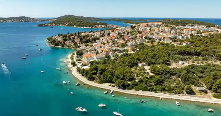 Vista aérea de una localidad costera de Croacia rodeada de aguas turquesas, pequeñas islas y embarcaciones en el mar Adriático.