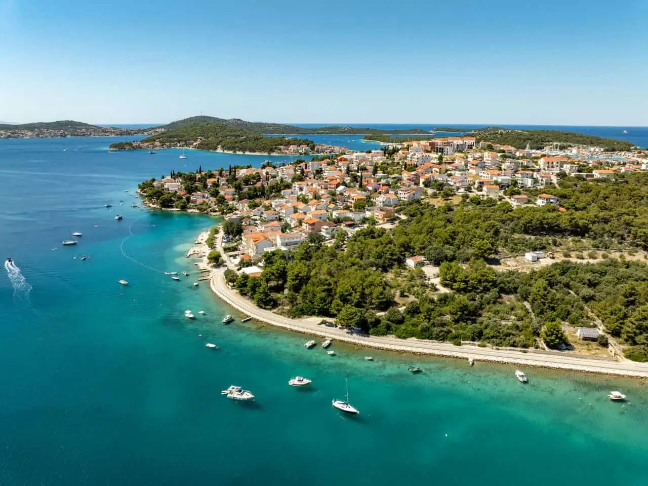 Vista aérea de una localidad costera de Croacia rodeada de aguas turquesas, pequeñas islas y embarcaciones en el mar Adriático.