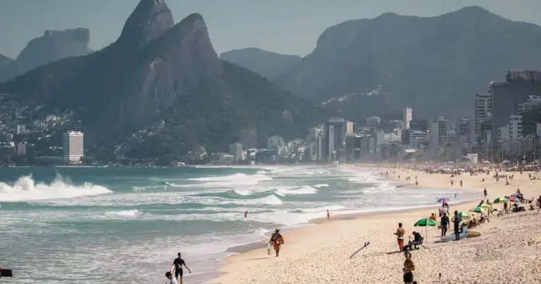 Playa de Ipanema en Río de Janeiro con familias y bañistas, y el Morro Dois Irmãos al fondo.