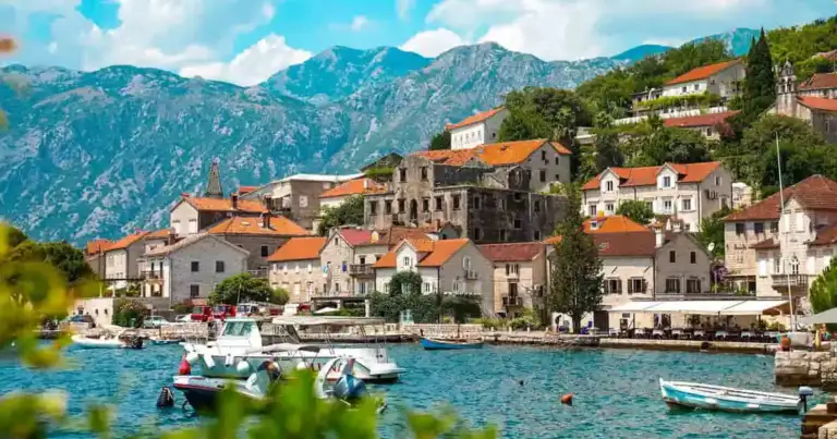 Pueblo costero de la bahía de Kotor, en Montenegro, con casas de piedra, barcos y montañas junto al mar Adriático.