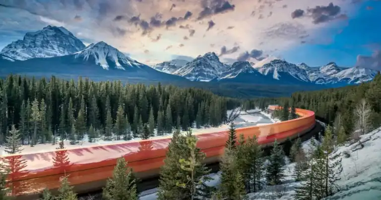 Tren recorriendo las Montañas Rocosas de Canadá entre bosques y cumbres nevadas durante el invierno.