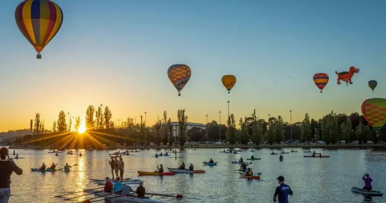 Globos aerostáticos sobre el lago Burley Griffin en Canberra al amanecer, con personas practicando kayak