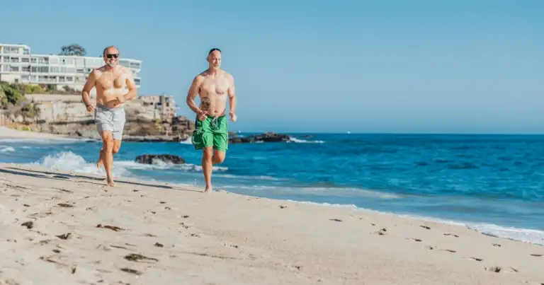 Dos hombres corren por la playa junto al mar en una ciudad costera
