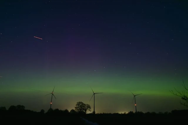 Auroras boreales: por qué una previsión favorable no garantiza una gran exhibición Aurora boreal tenue cerca del horizonte sobre un paisaje nocturno con aerogeneradores