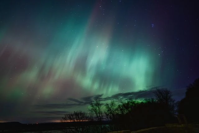 Auroras boreales y nubosidad: un factor clave al planificar el viaje Aurora boreal verde parcialmente cubierta por nubes sobre un paisaje oscuro