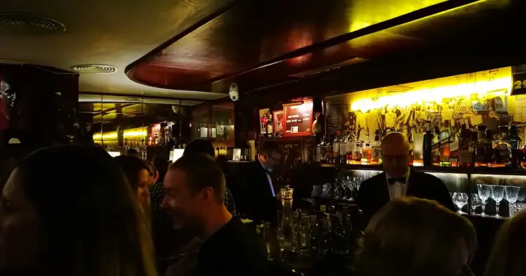 Barra de la coctelería Boadas de Barcelona por la noche, con clientes y un bartender de esmoquin detrás de la barra