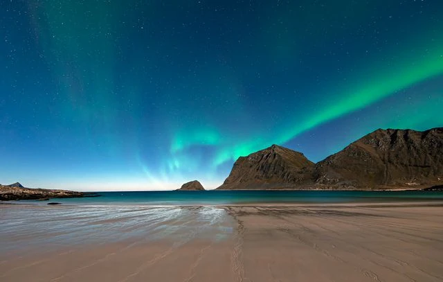 Errores al planificar un viaje para ver auroras boreales Aurora boreal sobre una playa y montañas bajo un cielo estrellado