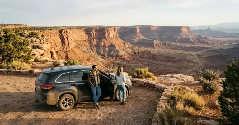 Pareja junto a un auto en un mirador de un paisaje de cañones del suroeste de Estados Unidos